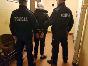 Policjanci stoją z zatrzymanym meżczyzną przed drzwiami do pomieszczenia dla osób zatrzymanych