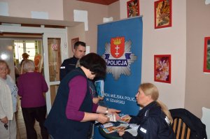 Policjantka rozdaje gadżety przy banerze z logo Policji