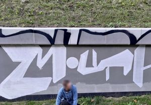 Mężczyzna kuca na tle muru z graffiti