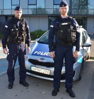 Zdjęcie dwóch policjantów umundurowanych przy radiowozie oznakowanym