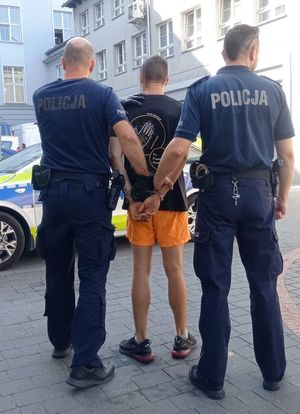 Umundurowani policjanci trzymają zatrzymanego mężczyznę w kajdankach