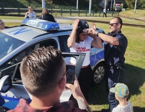 Oznakowany radiowóz i policjant, uczestnicy festynu