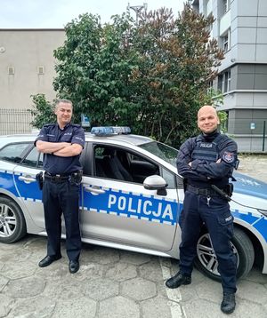 Dwaj policjanci stoją na tle radiowozu