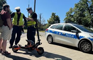 Policjanci ruchu drogowego kontrolują kierującego hulajnoga, w tle radiowóz