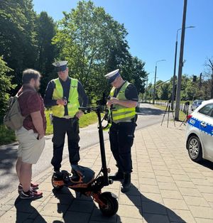 Policjanci ruchu drogowego kontrolują kierującego hulajnoga, w tle radiowóz