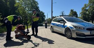 Policjanci ruchu drogowego kontrolują kierującego hulajnoga, w tle radiowóz