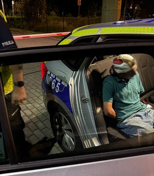 Policjant i zatrzymany mężczyzna, który siedzi w radiowozie
