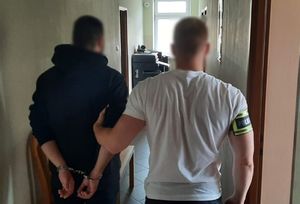Kryminalny prowadzi zatrzymanego mężczyznę