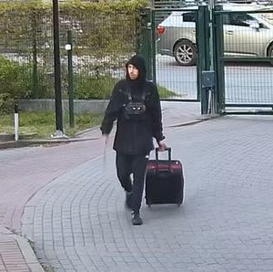 Mężczyzna ubrany na ciemno ciągnie walizkę na kółkach
