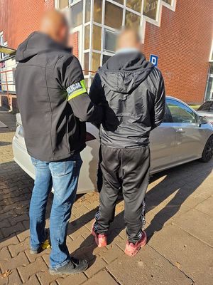 Policjant służby kryminalnej prowadzi zatrzymanego